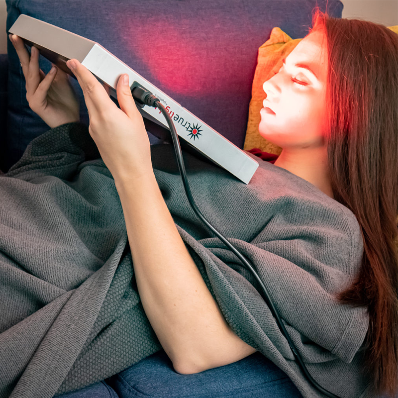 Woman covered with TrueLight Regenerative IR and FIR Blanket while using TrueLight Energy Square Light Therapy
